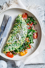 Wall Mural - Green spinach omelet with cheese, arugula and tomatoes on white plate, top view.