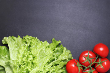 Green lettuce leaves red ripe tomatoes on a branch. Vegetables on a black textured background.