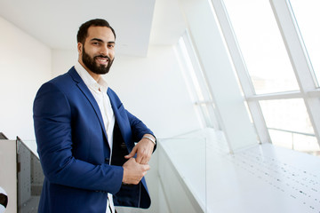 Successful handsome businessman in a blue suit at the workplace looks out the window, portrait of a manager at work