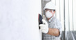 © amedeoemaja - man sand the wall with sandpaper, professional construction worker with mask, safety hard hat, gloves and protective glasses. interior building site, copy space background