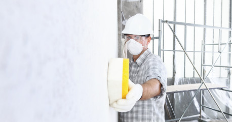 man builder using a sponge on  wall professional construction worker with mask, safety hard hat, gloves and protective glasses. interior building site, copy space background