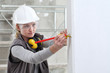 © amedeoemaja - woman construction worker work with meter tape and pencil, measure wall in interior building site, wearing helmet, glasses and hearing protection headphones