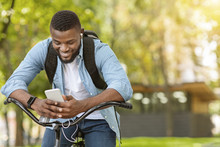 Outdoor Portrait Of Smiling Young Afro Man On Bike Using Smartphone
