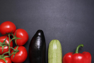 Green lettuce, red ripe tomatoes on a branch, fresh cucumbers and red bell peppers paprika. Vegetables on a black textured background.