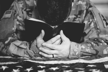 Greyscale shot of an American soldier mourning and praying with the Bible in his hands