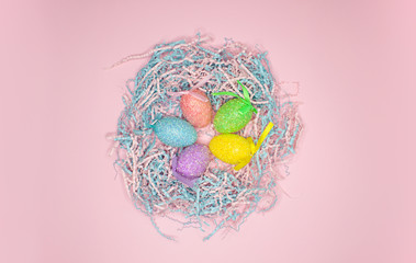 Colorful painted easter eggs in paper nest on pink background