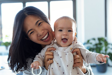 happy young mother with her baby daughter looking at camera while staying at home.