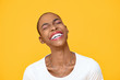 Happy optimistic African American woman laughing with eye closed isolated on colorful yellow background