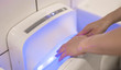 Female wet hand in modern vertical hand dryer in public restroom.