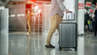 Close up of businessman carrying suitcase while walking through a passenger departure terminal in airport. Businessman traveler journey business travel.