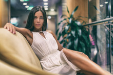 Asian Fashion Model Posing In White Dress On Luxurious Sofa In Cruise Ship. Beauty Young Woman High End Resort.