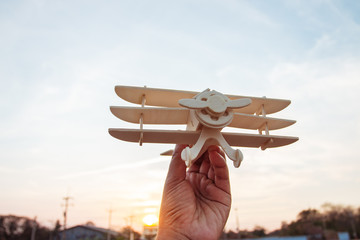 Freedom concept, human hand holding wooden plane on the sunset sky background