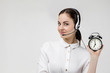 © Rychko Yevhen - Beautiful smiling woman consultant of call center in headphones holding alarm clock on gray background. female customer support operator with headset. save your time
