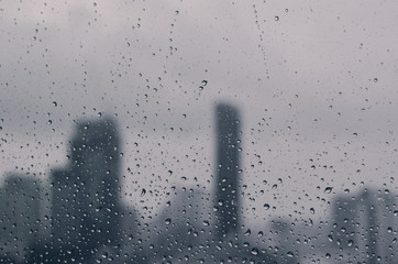 Wall Mural - Rain drop on glass window in monsoon season with blurred city buildings background.