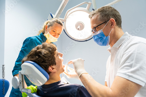 Obraz Dibond Profesjonalny chirurg dentysta i asystent wykonujący operacje dentystyczne w klinice z nowoczesnym wyposażeniem narzędzi