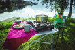 Folding camping table with items for cooking and food against a picturesque natural background in Norway. Summer vacation concept. A table with breakfast at a campsite on the background of a lake