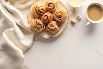 Wall Mural - top view of fresh homemade cinnamon rolls on marble surface with cup of coffee, brown sugar, condensed milk and silk cloth