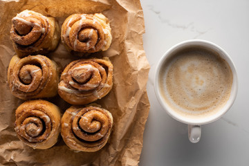 Wall Mural - top view of fresh homemade cinnamon rolls on parchment paper on marble surface with coffee