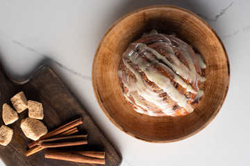 Wall Mural - top view of fresh homemade cinnamon roll on plate on marble surface with cutting board with brown sugar, cinnamon sticks