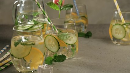 Wall Mural - Human hand puts mint branch in glass with summer healthy lemonade, cocktails of citrus infused water with lime lemon orange, ice and mint, diet detox beverages