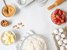 Frame Of Various Baking Ingredients - Flour, Eggs, Sugar, Butter, Fresh Strawberries, Nuts, Kitchen Utensils And Cupcake Baking Dish On White Background. Top View.
