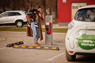 Wall Mural - Young mother with child charging electro car at the electric gas station.