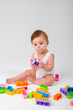 © Tina kids photo - baby with a pacifier in his mouth in white clothes sitting playing with a multi-colored constructor on a white background, space for text
