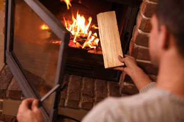 Canvas Print - Man putting dry firewood into fireplace at home, closeup. Winter vacation