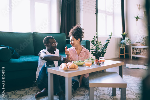 Fotomural Multiracial couple eating strawberry while having romantic dinner at home