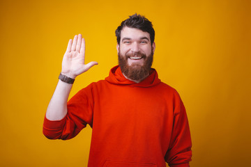 Wall Mural - Hi friends, smiling man with beard in red blouse making Hello gesture