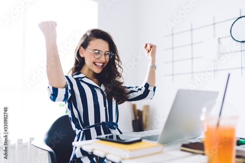 Fotomural Excited young woman sitting at table with laptop and celebrating success