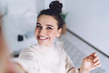 positive young woman using smartphone and having entertainment at home