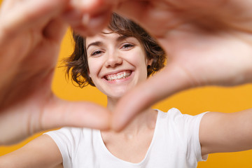 Wall Mural - Smiling young brunette woman girl in white t-shirt posing isolated on yellow orange background in studio. People lifestyle concept. Mock up copy space. Showing shape heart with hands heart-shape sign.