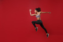 Side View Of Young African American Fitness Woman In Sportswear Posing Working Out Isolated On Red Wall Background Studio Portrait. Sport Exercises Healthy Lifestyle Concept. Jumping Like Running.