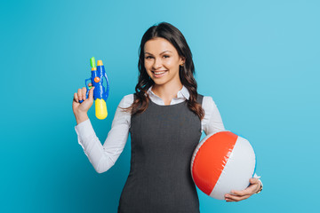 Wall Mural - happy businesswoman holding water gun and inflatable ball on blue background