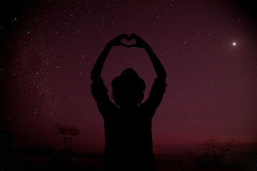 Wall Mural - silhouette of a girl holding heart-shape symbol for love on a starry night sky. my astronomy work.