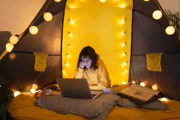 Wall Mural - little 11 year old girl using laptop under her home-made tent inside the living room.
