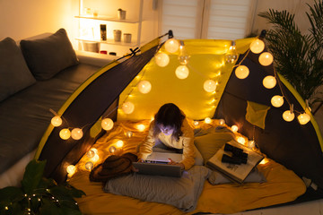 Wall Mural - little 11 year old girl using laptop under her home-made tent inside the living room.