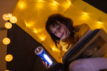 Wall Mural - young female child reading encyclopedia in a home made livingroom tent with light balls.