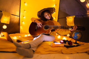 Wall Mural - little girl playing acoustic guitar under the tent in a living room.