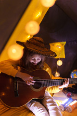 Wall Mural - little girl playing acoustic guitar under the tent in a living room.