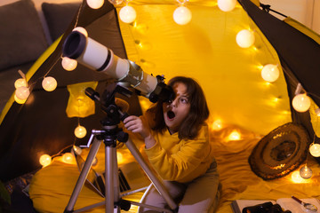 Wall Mural - small girl using telescope at home living room in a tent.