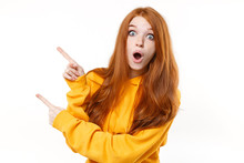 Shocked Young Redhead Woman Girl In Casual Yellow Hoodie Posing Isolated On White Background Studio Portrait. People Emotions Lifestyle Concept. Mock Up Copy Space. Pointing Index Fingers Aside Up.
