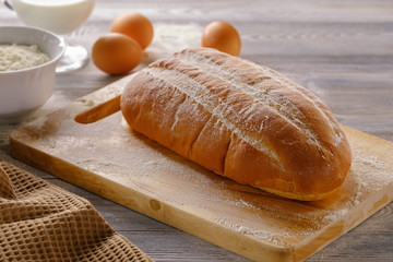 Fresh and tasty white loaf with crisp and ingredients for the recipe on a wooden table