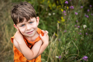 A young boy walks in the park among the tall grass and wildflowers and hugs himself, the boy is very fond of nature, the air is polluted in the city and it is difficult for him to breathe