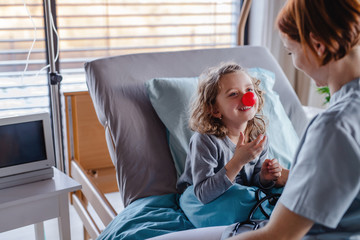 Wall Mural - Friendly female doctor examining small girl in bed in hospital.