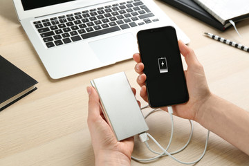 Woman charging mobile phone with power bank at wooden table, closeup