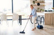 Portrait of senior woman with vacuum cleaner indoors at home, hoovering.