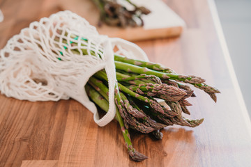 Fresh organic green asparagus in a rope bag on wooden background