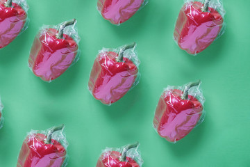 Pattern of recycling and environment concept: fresh red paprika in plastic package. Bell pepper wrapped in plastic cellophane in green background